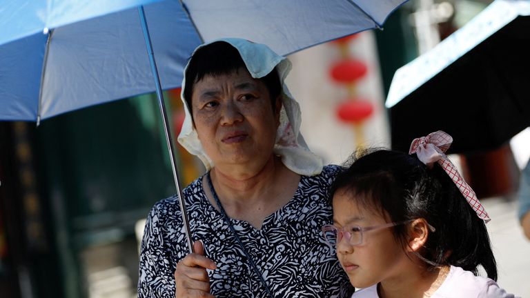 A person wearing a towel on her head holds an umbrella, as she walks on a street, amid a red alert for heatwave in Beijing, China