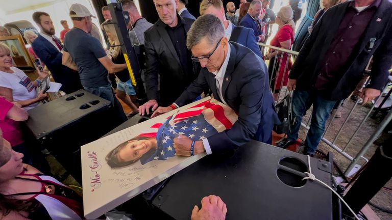 FILE - Michael Flynn, a retired three-star general who served as President Donald Trump&#39;s national security advisor, autographs a picture of a girl wrapped in an American flag during the ReAwaken America Tour at Cornerstone Church in Batavia, N.Y., Aug. 12, 2022. Flynn, one of the tour&#39;s founders and its star, warned the crowd that they were in the midst of a "spiritual war" and urges people to get involved in local politics." (AP Photo/Carolyn Kaster)