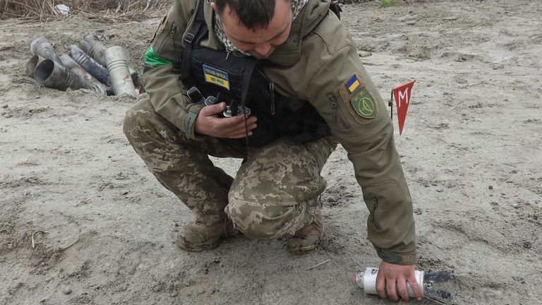 A Ukrainian soldier collects an unexploded part of a cluster bomb near the village of Motyzhyn in April 2022