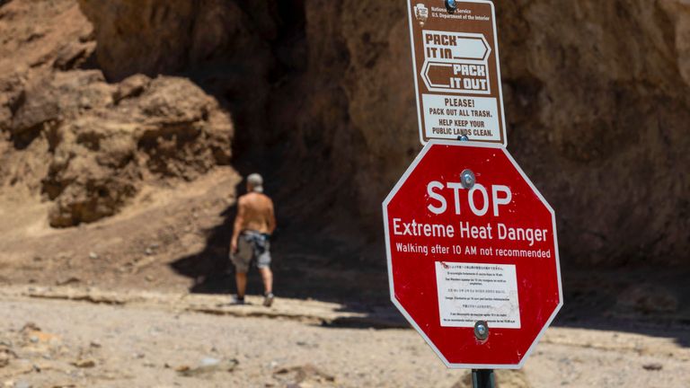 Kaliforniya'daki Death Valley Ulusal Parkı'nda 11 Temmuz 2023'te Altın Kanyon yolunun başlangıcında yürüyüşçüleri aşırı sıcak konusunda uyaran bir tabelanın yanından geçen bir yürüyüşçü. 18 Temmuz Salı günü Los Angeles bölgesinden 71 yaşındaki bir adam, sıcaklık 121 derece (49 Santigrat) veya üzerine çıktığında ve korucuların ısının bir faktör olduğundan şüphelenmesi nedeniyle patika başında öldü. Ulusal Park Servisi Çarşamba günü yaptığı açıklamada.  (AP Fotoğrafı/Ty ONeil)