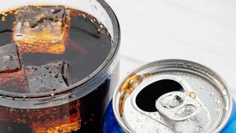 Open aluminum can and glass of cola with ice on white. Image: iStock