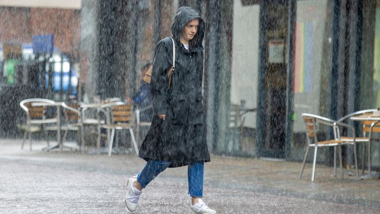 A woman walks down a street during a heavy downpour of rain in Belfast. Picture date: Monday July 31, 2023.