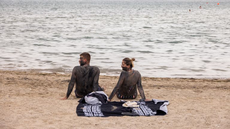 A couple covered in mud that is believed to be curative sit at the Queen&#39;s beach in Nin