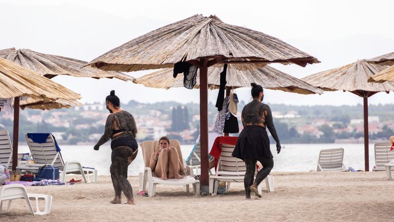 Women walk covered with mud that is believed to be curative at the Queen&#39;s Beach in Nin