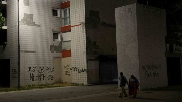 Residents walk past phrases written on walls of buildings at a neighbourhood where Nahel was killed, in Nanterre
