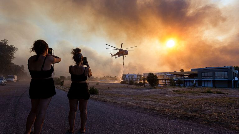 People take photos of a firefighting helicopter filling water from a pool, in the village of Gennadi, on the island of Rhodes, Greece, July 25, 2023. REUTERS/Nicolas Economou
