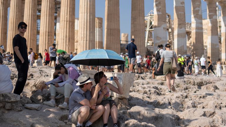 A tourist drinks water as she and a man sit under an umbrella in front of the five century BC Parthenon temple at the Acropolis hill during a heatwave in Greece
Pic:AP