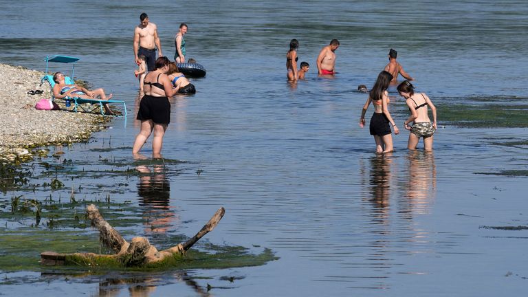 People cool-off on the banks of the Ticino river at the Ponte delle Barche (boats bridge) in Bereguardo, near Milan, Italy, Tuesday, July 11, 2023. An intense heat wave has reached Italy, bringing temperatures close to 40 degrees Celsius in many cities across the country. (AP Photo/Antonio Calanni)