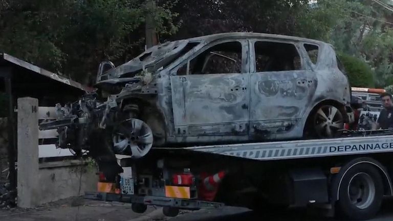 A burnt-out car is removed from the scene