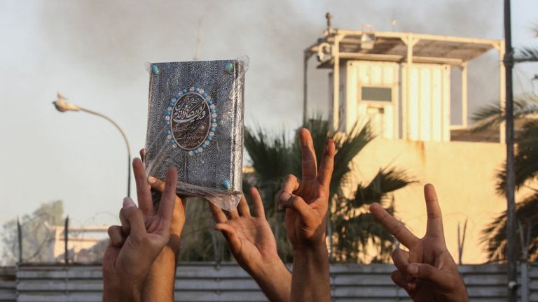 İsveç büyükelçiliğinden dumanlar yükselirken bir protestocu Kuran'ın bir kopyasını elinde tutuyor