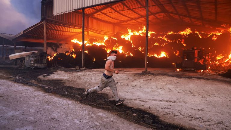 A young man runs next to a burning farm, as a wildfire burns in Sesklo, in central Greece, July 26, 2023. REUTERS/Alexandros Avramidis