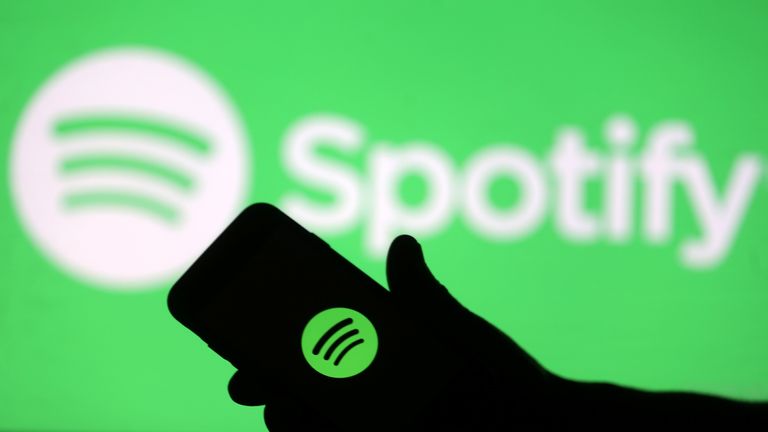 A smartphone is seen in front of a screen projection of Spotify logo, in this picture illustration