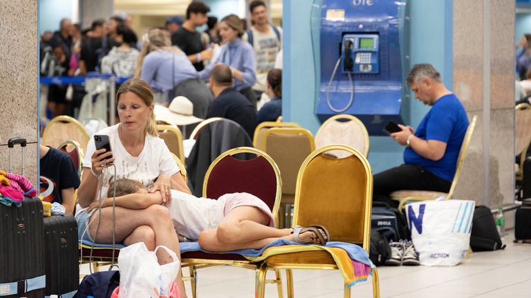 A woman checks her phone as tourists wait for departing planes at the airport, after being evacuated following a wildfire on the island of Rhodes, Greece, July 24, 2023. REUTERS/Nicolas Economou
