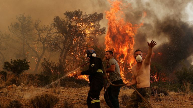 Yunanistan, Atina yakınlarındaki Vlyhada köyü yakınlarında yanan bir orman yangınını söndürmeye çalışan bir itfaiyeciye yardım eden adamlar, 19 Temmuz 2023. REUTERS/Stelios Misinas TPX GÜNÜN TPX GÖRÜNTÜLERİ