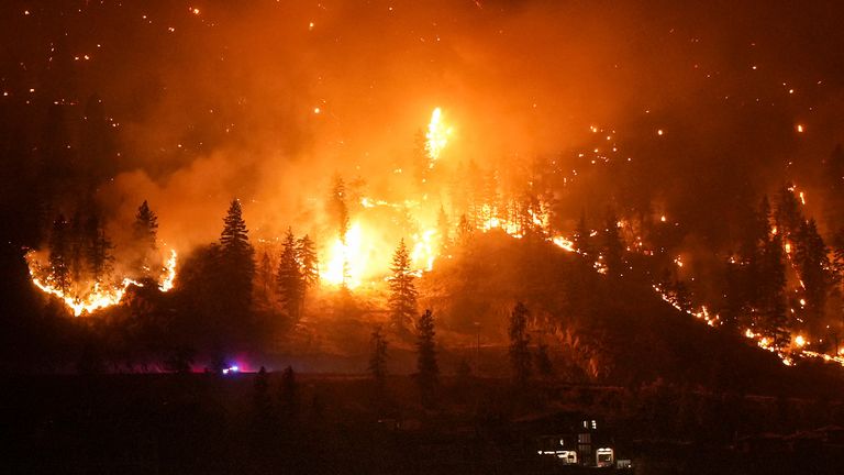The McDougall Creek wildfire burns on the mountainside above a lakefront home in West Kelowna, Canada on Friday, Aug. 18, 2023. (Darryl Dyck/The Canadian Press via AP)