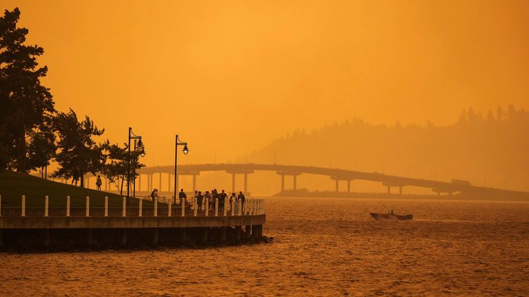 A person travels in a boat past people walking on the boardwalk in British Columbia. Pic: AP