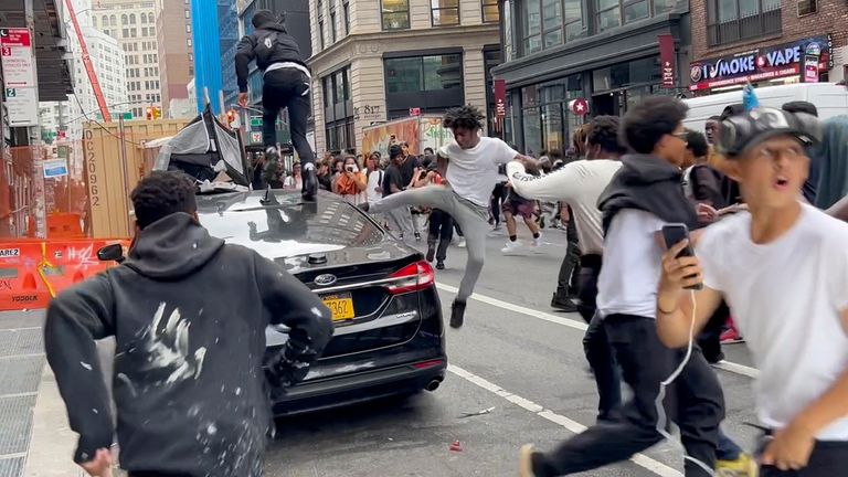 People jump and kick a car as a crowd runs through the street on Broadway near Union Square. Pic: AP
