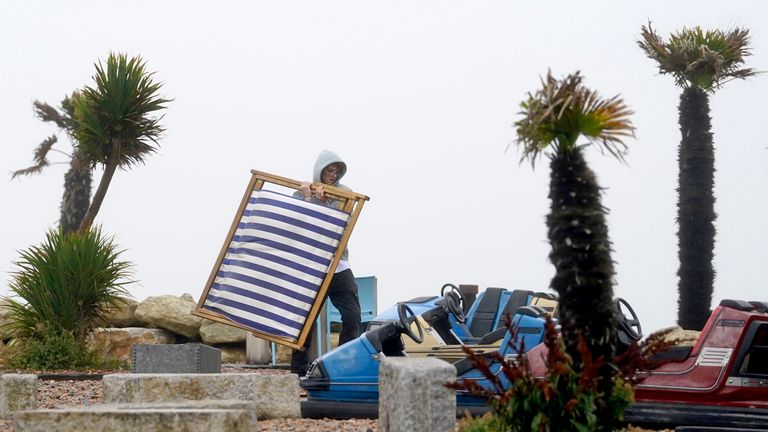 A man clears empty deckchairs from the beach during bad weather in Folkestone, Kent. Picture date: Monday July 31, 2023.

