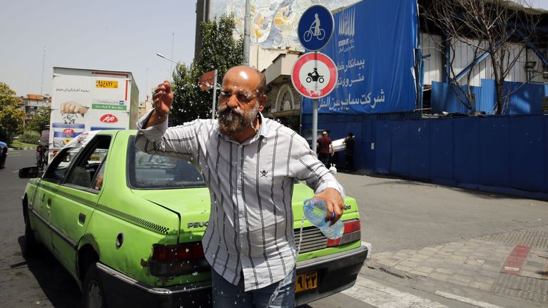 An Iranian Taxi driver splashes water into his face to cool off in a downtown street during a hot and sunny day in Tehran, Iran