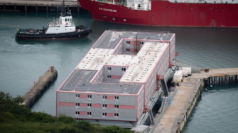 A tug boat passes the Bibby Stockholm accommodation barge at Portland Port in Dorset, which will house up to 500 people. The Home Office have said around 50 asylum seekers would board the Bibby Stockholm, with the numbers rising to its maximum capacity over the coming months, despite safety concerns raised by some of the county&#39;s Conservative MPs and locals. Picture date: Thursday August 3, 2023.