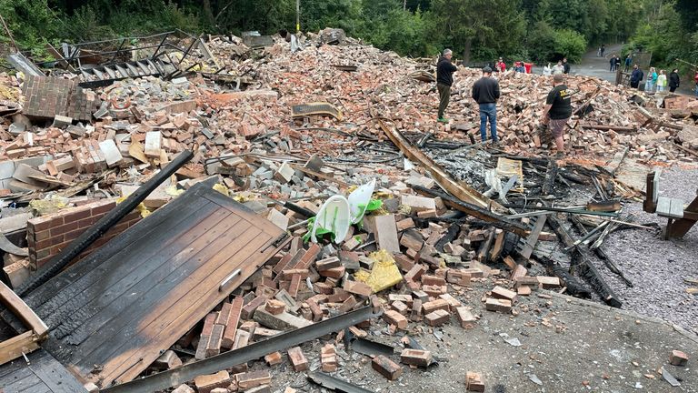 People inspect the rubble remains as they gather at The Crooked House