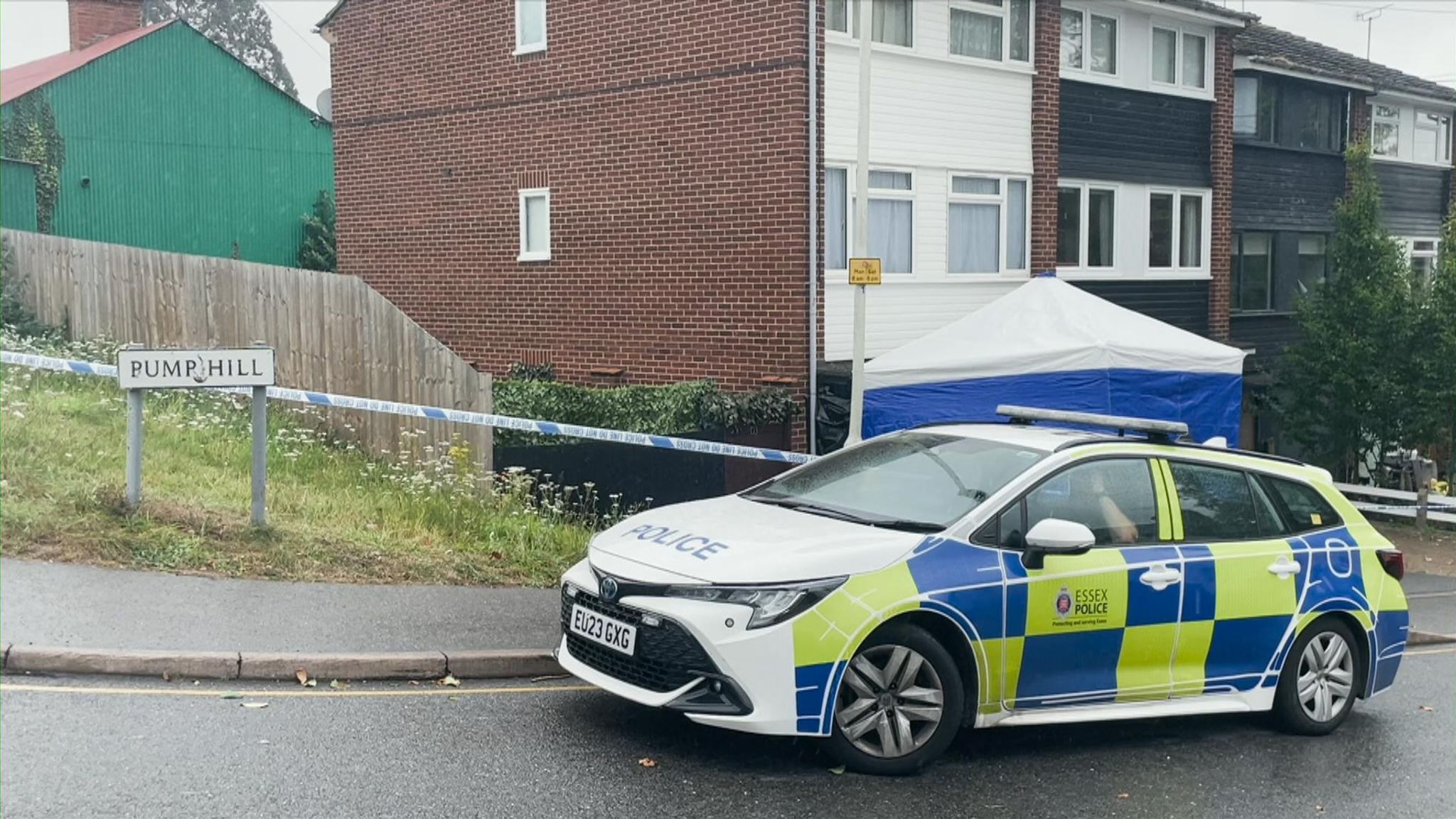  A police car is parked in front of a house that is cordoned off with police tape. A tent has been erected in the front yard and a鑑識人員 is working at the scene.