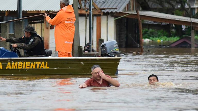 Police officers check a house as residents wade through a flooded street after floods caused by a cyclone in Passo Fundo, Rio Grande do Sul state, Brazil, Monday, Sept.4, 2023. Rio Grande do Sul Gov. Eduardo Leite said that about 60 cities had been battered by the storm, which was classified as an extratropical cyclone. (AP Photo/Diogo Zanatta-Futura Press)