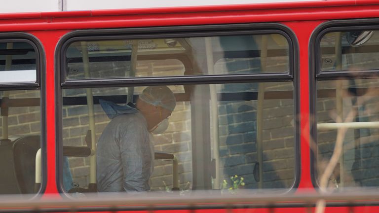 A forensic officer works on a double decker bus behind the police cordon