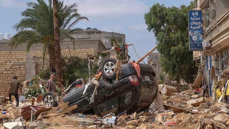 A man stands next to a damaged car, after a powerful storm and heavy rainfall hit Libya, in Derna.