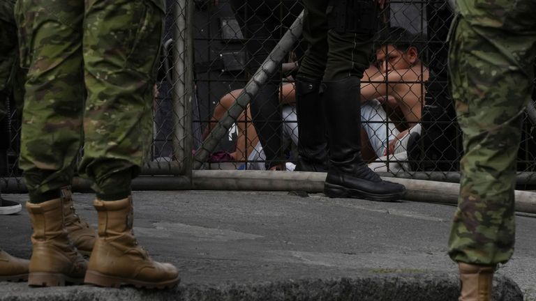 A juvenile looks out from behind a guarded area of the Virgilio Guerrero detention center after inmates were evacuated to a patio due to a fire at the center set by a group of detainees, in Quito, Ecuador, Thursday, Aug. 31, 2023. (AP Photo/Dolores Ochoa)
