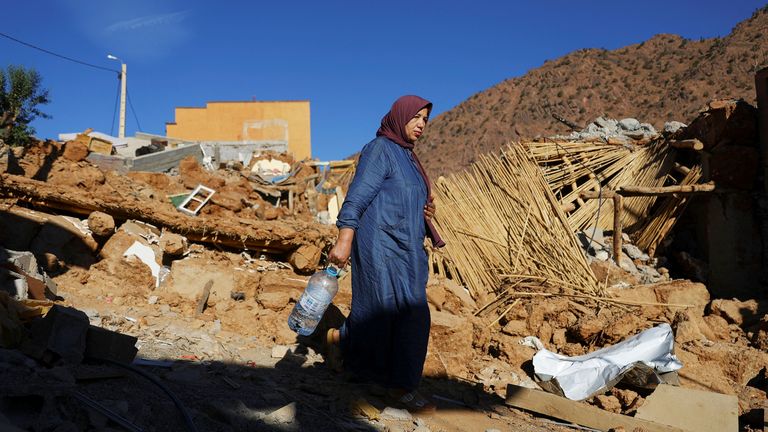 A woman carries a bottle, as she walks near rubble, in the aftermath of a deadly earthquake, in a hamlet on the outskirts of Talaat N&#39;Yaaqoub, Morocco
