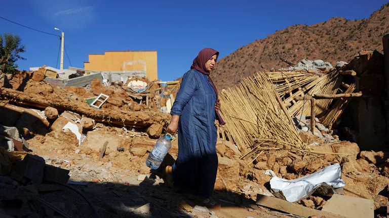 A woman carries a bottle, as she walks near rubble, in the aftermath of a deadly earthquake, in a hamlet on the outskirts of Talaat N&#39;Yaaqoub, Morocco
