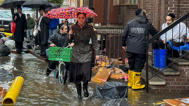 Pedestrians walk along a flooded sidewalk,