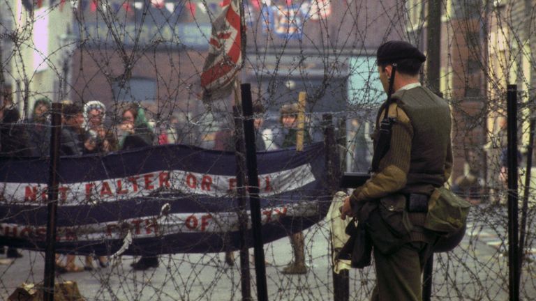Troops on duty beside barbed wire barriers in the Falls Road area of Belfast in 1969