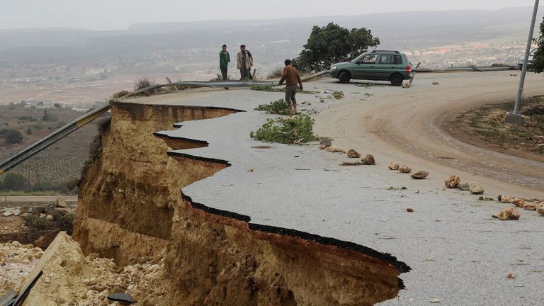 People stand in a damaged road as a powerful storm and heavy rainfall flooded hit Shahhat city, Libya
