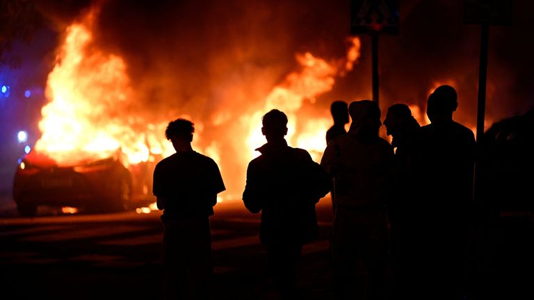 People are silhouetted as cars burn during a riot in Malmo, Sweden