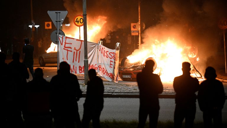 People are silhouetted as cars burn during a riot in Malmo, Sweden