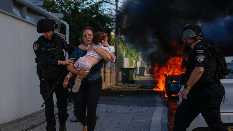 Police officers evacuate a woman and a child from a site hit by a rocket fired from the Gaza Strip, in Ashkelon, southern Israel, Saturday, Oct. 7, 2023. The rockets were fired as Hamas announced a new operation against Israel. (AP Photo/Tsafrir Abayov)
