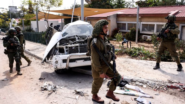 Israeli soldiers walk past a damaged car in Kibbutz Kfar Aza, in southern Israel, October 10, 2023. REUTERS/Ronen Zvulun