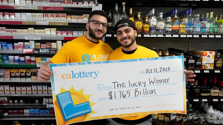 Jonathan Khalil, left, and Chris Khalil, sons of the store co-owners, hold up a ceremonial check presented to them by lottery officials at the Midway Market & Liquor store, Thursday, Oct. 12, 2023, in Frazier Park, Calif., where a $1.765 billion winning Powerball ticket was sold.  (AP Photo/Marcio Jose Sanchez)