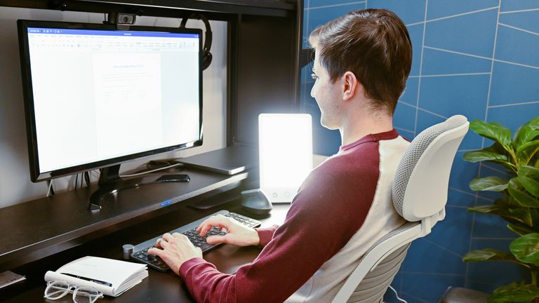A young man is using a sunlight simulator lamp in his home office to combat the effects of Seasonal Affective Disorder. Pic: iStock