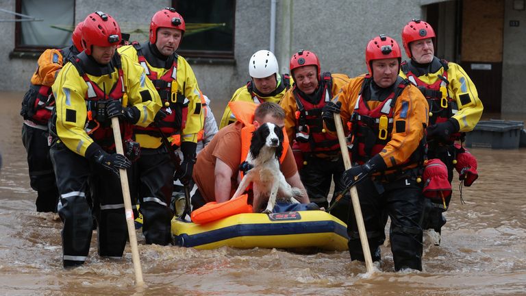 A man with a dog sits on dinghy as emergency services assist in the evacuation of people from their homes in Brechin