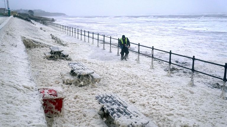 A man walks through sea foam in Seaburn, Sunderland,  as Storm Babet batters the country 
