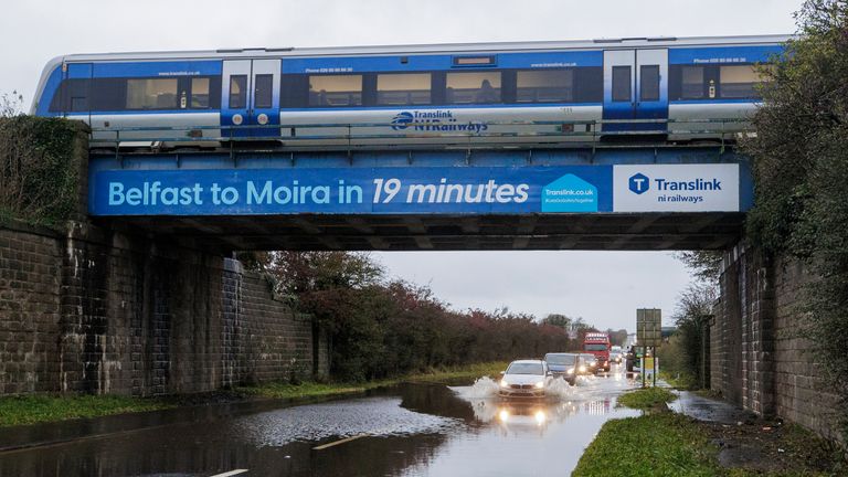 A car drives through a flooded area under a railway bridge as a train passes overhead, on the A26 outside the village of Moira in Northern Ireland