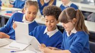 Elementary school children wearing blue school uniforms using digital tablets at desk in classroom stock photo