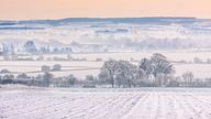 As sunset approaches the mist hangs in valleys over snowy, Oxfordshire fields near Wittenham Clumps