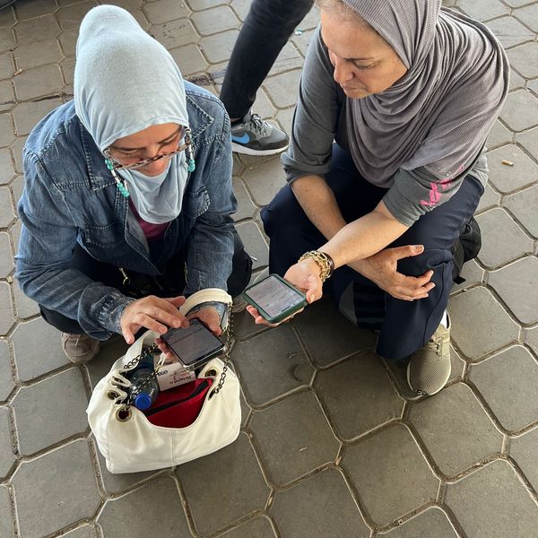 Two people crouching looking at phones in Gaza