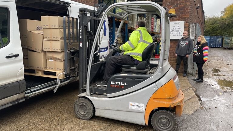 Simon and Zoe stand alongside a forklift truck loading up boxes of formula milk 