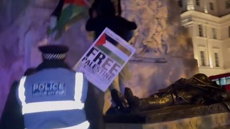 An officer approaches a pro-Palestinian protester who is climbing off the monument