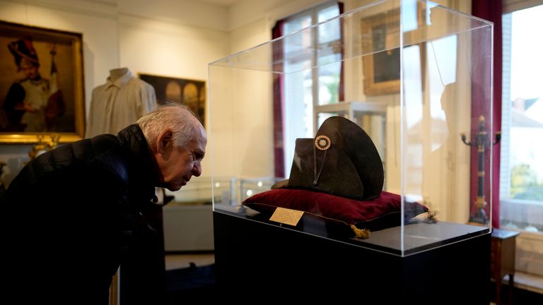 A visitor watches one of the signature broad, black hats that Napol..on wore when he ruled 19th century France and waged war in Europe on display at Osenat&#39;s auction house in Fontainebleau, south of Paris, Friday, Nov. 17, 2023. The hat is tipped to fetch more than half a million euros (dollars) at the auction Sunday of Napoleonic memorabilia patiently collected by a French industrialist. (AP Photo/Christophe Ena)